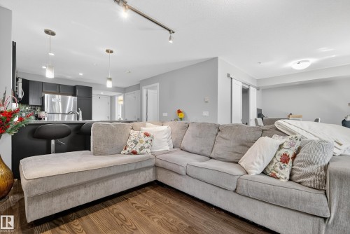 Open-concept living area with wood-finish flooring, track lighting, and a breakfast bar with pendant lights - #107 1031 173 St Sw, Edmonton, AB 
