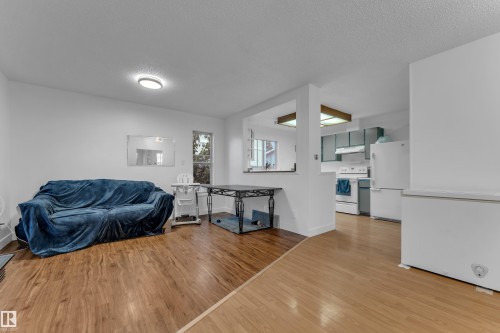 Open-concept living area with wood-finish flooring, a pass-through to the kitchen, and a window - 442 Kirkpatrick Crescent Nw, Edmonton, AB 