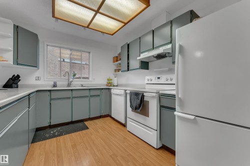 Kitchen featuring wood-finish flooring, a double basin sink with a gooseneck faucet, a ceiling-mounted light fixture, and white appliances - 442 Kirkpatrick Crescent Nw, Edmonton, AB 