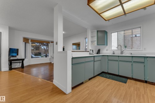 Kitchen featuring light wood-finish flooring, L-shaped cabinetry with a white countertop, and a stainless steel sink with a gooseneck faucet - 442 Kirkpatrick Crescent Nw, Edmonton, AB 