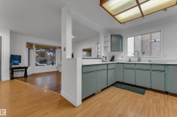 Kitchen featuring light wood-finish flooring, L-shaped cabinetry with a white countertop, and a stainless steel sink with a gooseneck faucet - 