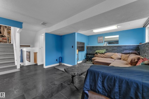 Spacious room featuring dark tile flooring, a staircase with carpeted treads, and a partial accent wall with stacked stone - 442 Kirkpatrick Crescent Nw, Edmonton, AB 