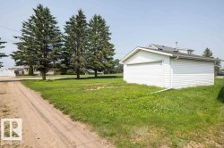 Detached garage featuring white vinyl siding, a white garage door, and a gray shingled roof - 