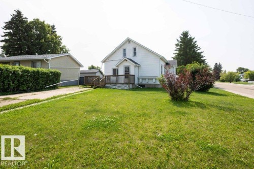 Expansive front yard with a large grassy area, mature shrubbery, and a paved driveway - 10940 100A Ave, Westlock, AB - Outdoor