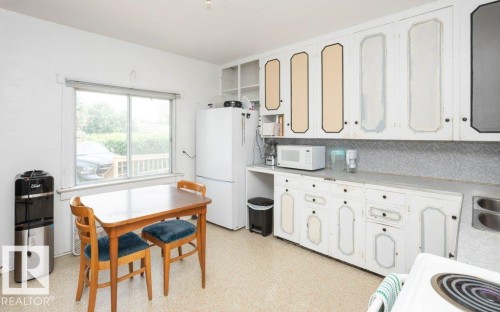 Kitchen featuring a window overlooking exterior surroundings, upper and lower cabinetry, a double basin sink, and a refrigerator - 10940 100A Ave, Westlock, AB - Indoor Photo Showing Kitchen