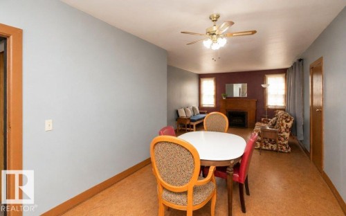 Open-concept living area featuring a fireplace with a wood mantle, a ceiling fan with integrated lighting, and light brown flooring - 10940 100A Ave, Westlock, AB - Indoor Photo Showing Other Room With Fireplace