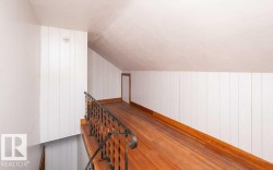Loft area featuring wood-finish flooring, white vertical paneling, and an ornate metal railing - 