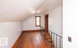 Upper-level hallway featuring wood-finish flooring, white vertical wall paneling, a sloped ceiling, and a black wrought iron staircase railing - 
