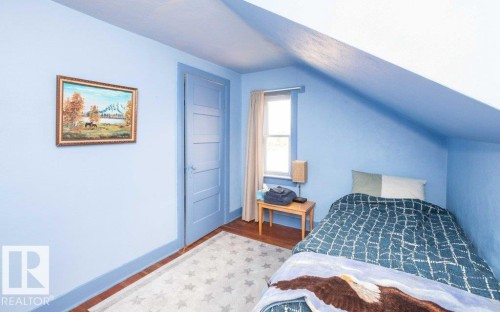 Room featuring wood-finish flooring, a paneled door, sloped ceiling detail, and a window with natural light - 10940 100A Ave, Westlock, AB - Indoor Photo Showing Bedroom