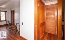 Upper level hallway featuring wood-finish flooring, white vertical paneling, and natural wood trim around windows and doorways - 