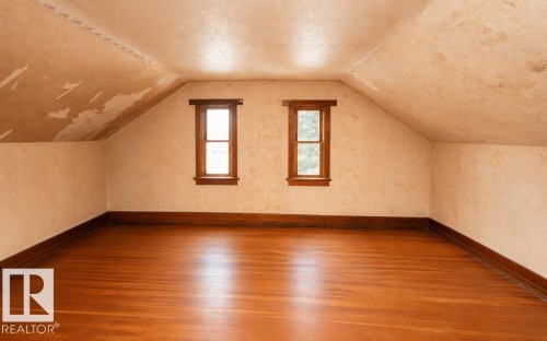 Spacious attic room featuring wood-finish flooring and two single-pane windows with wood trim - 10940 100A Ave, Westlock, AB - Indoor Photo Showing Other Room