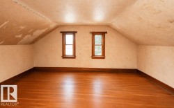 Spacious attic room featuring wood-finish flooring and two single-pane windows with wood trim - 