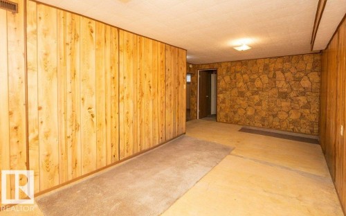 Room featuring wood-paneled walls, stone-patterned accent wall, and a textured ceiling - 10940 100A Ave, Westlock, AB - Indoor Photo Showing Other Room