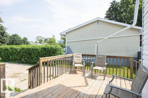Wooden deck with railing overlooking a concrete patio and expansive green hedge - 10940 100A Ave, Westlock, AB - Outdoor With Deck Patio Veranda With Exterior