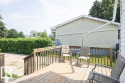 Wooden deck with railing overlooking a concrete patio and expansive green hedge - 