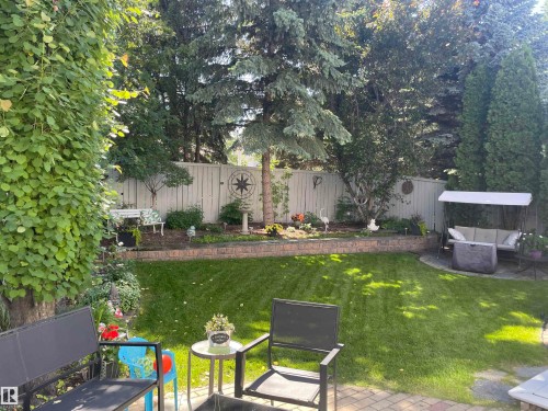 Manicured backyard featuring a lush lawn, mature perimeter trees, a stone retaining wall, and a full privacy fence - 716 Hendra Crescent Nw, Edmonton, AB - Outdoor With Backyard