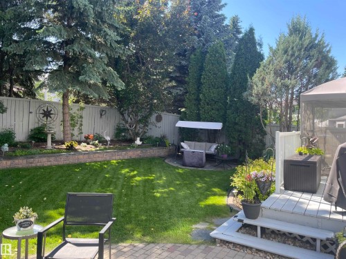 Expansive backyard featuring a lush lawn, mature trees, a raised garden bed with retaining wall, a paved patio area, and a wood deck - 716 Hendra Crescent Nw, Edmonton, AB - Outdoor With Backyard