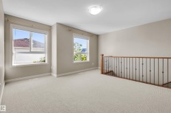 Carpeted open area with two windows, a light fixture, and a wood and wrought iron staircase railing - 