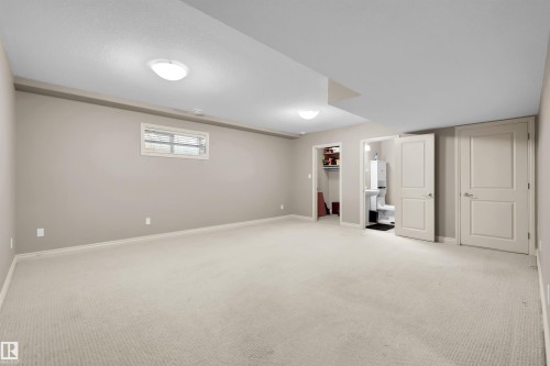 Spacious carpeted room featuring neutral wall tones, recessed lighting, a window with blinds, and white panel doors - #5 5120 164 Av Nw, Edmonton, AB 