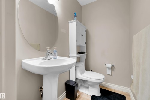Pedestal sink with chrome faucet, oval wall mirror, toilet with white over-the-toilet cabinet, and light-colored flooring - #5 5120 164 Av Nw, Edmonton, AB 