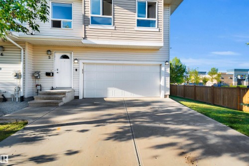 Cream-colored siding exterior, attached garage with a white door, concrete driveway, front entrance with concrete steps, and a wooden privacy fence - #5 5120 164 Av Nw, Edmonton, AB 
