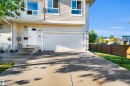 Cream-colored siding exterior, attached garage with a white door, concrete driveway, front entrance with concrete steps, and a wooden privacy fence - #5 5120 164 Av Nw, Edmonton, AB 