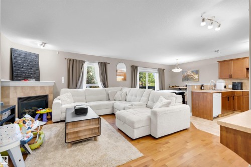 Living area featuring a gas fireplace with a tile surround, wood-finish flooring, and a kitchen with wood cabinetry and a dishwasher - #5 5120 164 Av Nw, Edmonton, AB 