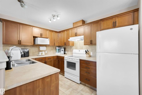 L-shaped kitchen with wood-finish cabinetry, beige countertops, and tile flooring - #5 5120 164 Av Nw, Edmonton, AB 