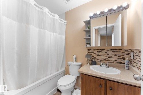 Bathroom vanity featuring a light-colored countertop with an integrated sink, wood-finish cabinetry, and a mosaic tile backsplash - 173 Cornell Court Nw, Edmonton, AB - Indoor Photo Showing Bathroom