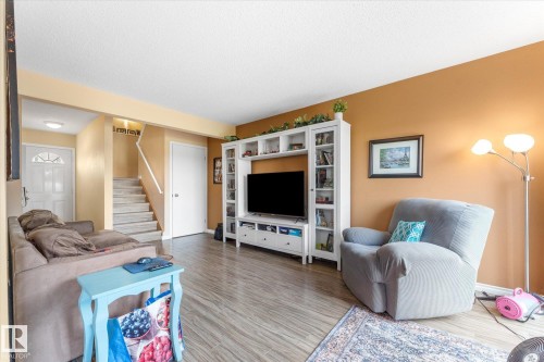 Living area featuring wood-finish flooring, a white media console with built-in shelving, a staircase with white railings, and a white entry door with frosted glass - 173 Cornell Court Nw, Edmonton, AB - Indoor Photo Showing Living Room