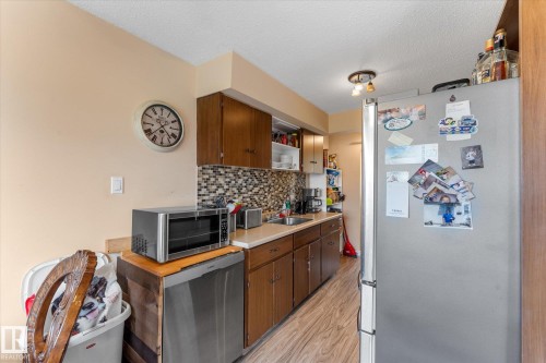 Kitchen featuring wood-finish flooring, wood cabinetry, a tiled backsplash, and a stainless steel refrigerator - 173 Cornell Court Nw, Edmonton, AB - Indoor Photo Showing Kitchen