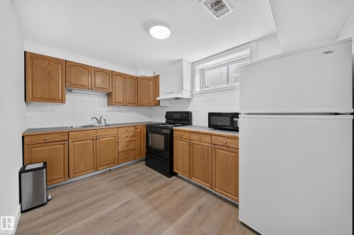 Wood-finish flooring, white subway tile backsplash, wood cabinetry, built-in range, and a window for natural light - 5204 97A Avenue Nw, Edmonton, AB 
