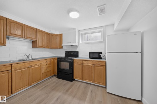 Kitchen featuring wood-finish cabinetry, subway tile backsplash, a stainless steel double-basin sink, and a black electric range - 5204 97A Avenue Nw, Edmonton, AB 
