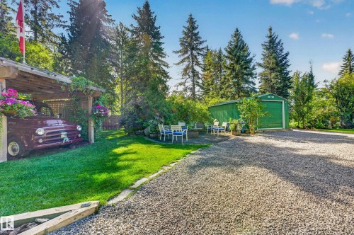 Gravel driveway with a green storage shed, covered parking structure, and a lawn area with mature trees - 51 Itaska Beach, Rural Leduc County, AB 