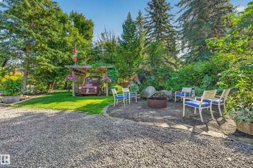 Gravel driveway leading to a stone patio with a fire pit, surrounded by mature trees and lush landscaping - 51 Itaska Beach, Rural Leduc County, AB 