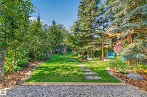 Lush landscaping with mature trees, a manicured lawn, and stone paver pathway - 51 Itaska Beach, Rural Leduc County, AB 