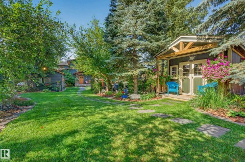 Manicured lawn, mature trees, stone paver pathway, detached outbuilding with a covered porch, and exterior lighting fixture - 51 Itaska Beach, Rural Leduc County, AB 