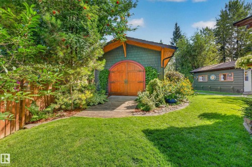 Landscaped grounds featuring a wooden fence, lush lawn, and mature plantings - 51 Itaska Beach, Rural Leduc County, AB 