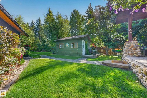 Manicured lawn with a stone pathway, a detached green shed, mature trees, and a flagstone patio with a stone-clad pillar - 51 Itaska Beach, Rural Leduc County, AB 