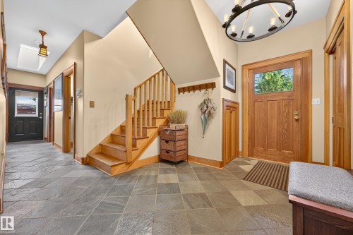 Slate tile flooring, natural wood staircase, wood front door with glass panel, wood trim, and a decorative circular chandelier - 51 Itaska Beach, Rural Leduc County, AB 