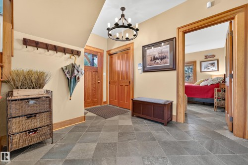 Foyer featuring slate tile flooring, a wood-paneled entry door, wood trim, and a black chandelier - 51 Itaska Beach, Rural Leduc County, AB 