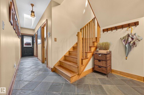 Entryway featuring natural stone-finish flooring, wood staircase, wood railing, wood door frames, and a skylight - 51 Itaska Beach, Rural Leduc County, AB 