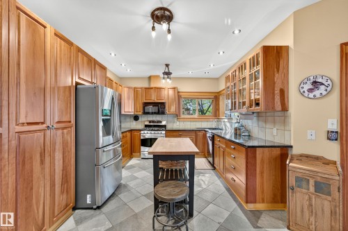 Kitchen featuring extensive wood cabinetry, stainless steel appliances, dark countertops, and a tiled floor - 51 Itaska Beach, Rural Leduc County, AB 