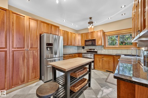 Spacious kitchen featuring extensive wood cabinetry, stainless steel appliances, dark stone countertops, and a central island with a wood-finish top - 51 Itaska Beach, Rural Leduc County, AB 