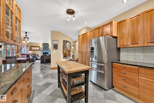 Kitchen featuring wood cabinetry, stainless steel refrigerator, dark stone countertops, and checkerboard floor tiling - 51 Itaska Beach, Rural Leduc County, AB 
