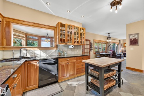 Wood cabinetry with glass-front upper cabinets, dark stone countertops, black appliances, and a central island with a wood-finish top - 51 Itaska Beach, Rural Leduc County, AB 