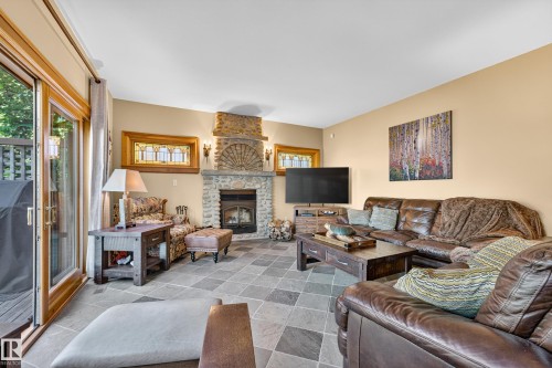 Stone-clad fireplace with a hearth, tile flooring, sliding glass patio doors, and stained-glass accent windows - 51 Itaska Beach, Rural Leduc County, AB 