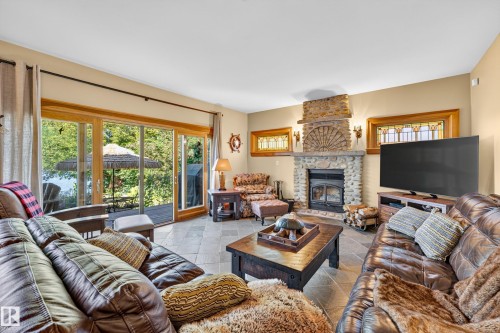 Stone fireplace with hearth, tile flooring, glass sliding doors, and stained glass window accents - 51 Itaska Beach, Rural Leduc County, AB 