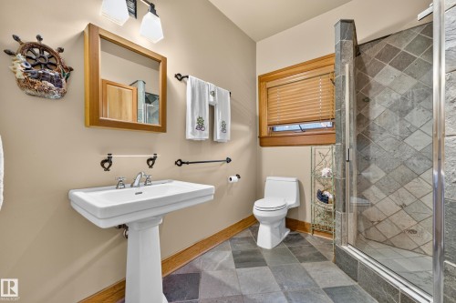 Pedestal sink, wood-framed mirror, walk-in shower with glass enclosure, diagonal tile flooring, and a natural wood trim window - 51 Itaska Beach, Rural Leduc County, AB 