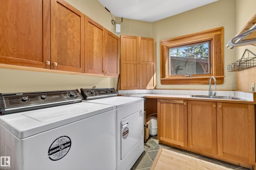 Laundry area featuring wood cabinetry, a built-in sink, stone tile flooring, and a window - 51 Itaska Beach, Rural Leduc County, AB 